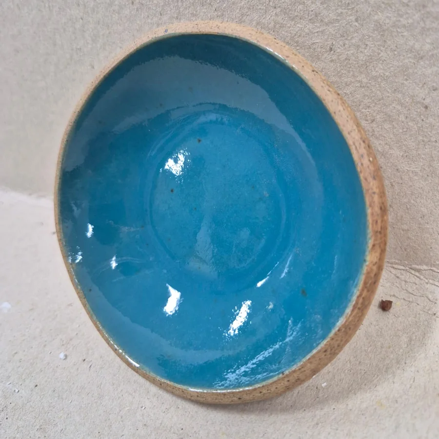 Prato fundo de cerâmica com esmalte azul brilhante por dentro e borda de barro aparente, visto de cima